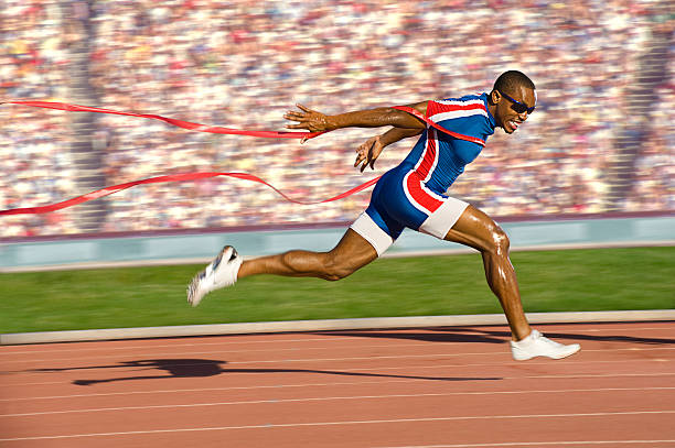 Sprinter Crossing the Finish Line African-American sprinter crossing the finish line and breaking the tape. Horizontally framed shot. track and field athlete stock pictures, royalty-free photos & images