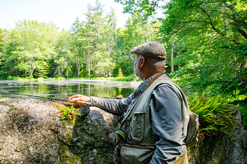 A mature male fly-fishing angler fishing for trout.  He is wearing waders and a fishing vest.