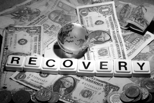 A globe rests on cash with the word recovery before it.