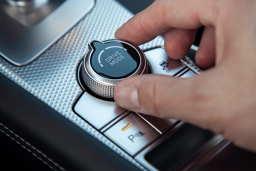 A man turning a drive mode dial in the interior of a luxury car.