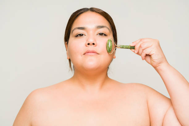 istock Large big woman using a jade roller in a studio background for soft skin 1520377771