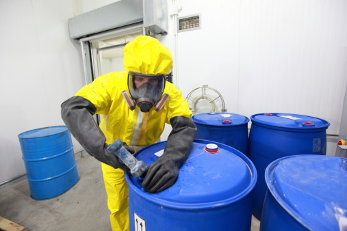 Fully protected in yellow uniform,mask,and gloves professional filling barrel with chemicals