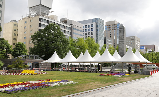 Sapporo, Japan - May 30, 2023: Entertainment tents line a section of Odori Park ahead of outdoor events. This public park hosted festivities during the 1972 Winter Games. Background shows buildings along Odori Avenue. Spring afternoon in Chuo Ward.