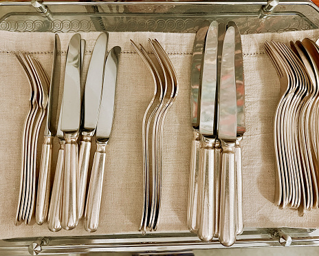 Horizontal high angle closeup photo of a collection of polished silverware on a linen cloth on a silver tray.
