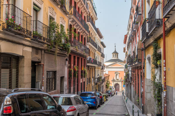Madrid, Spain - June 27, 2023: View of some neighbors passing through the quiet and traditional neighborhood of Lavapies, at the end of the street you can see the Church of San Lorenzo. Lavapiés is a historic neighborhood in the city of Madrid, Spain. Lavapiés was considered for a long time the most \