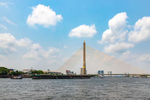 Bangkok,Thailand - Mar 30, 2023: Sand boats are sailing along the Chao Phraya River. Bangkok's main river going through the Rama VIII Bridge in the daytime the sky is beautiful. It is a way of life.