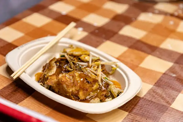 Photo of Hoy-Tod Delicious Thai food made from oysters, flour, egg and fried until crispy. Famous Thai food. Put in a disposable paper plate on a table covered with plastic checkered cloth. Selective focus.