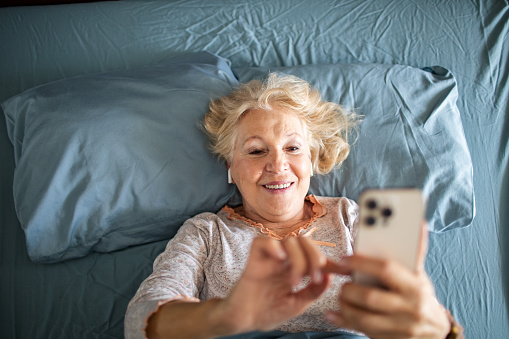 Close up of a Senior woman using a phone while lying down in a bedroom