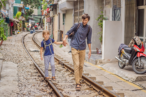 Father and son travelers walk around railway paths which go through residential area in Hanoi city. Hanoi Train Street is a famous tourist destination. Vietnam reopens after coronavirus quarantine COVID 19.