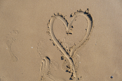 Drawing heart shape love concept on sand at the beach with vacation holiday summer travel background. Heart shape and footprint on wet sand.