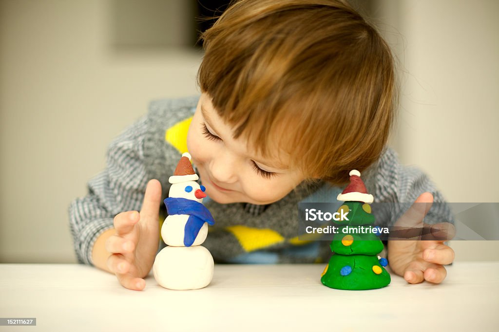 Little boy playing with Christmas themed clay figures a child making a snowman and christmas tree of plasticine Christmas Stock Photo