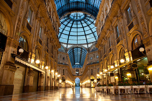 Milan Luxuous shopping mall Symmetrical night shot of the famous Galleria Vittorio Emanuele II in Milan, Italy, showing the spectacular view of an almost golden gate to luxury galleria vittorio emanuele ii stock pictures, royalty-free photos & images