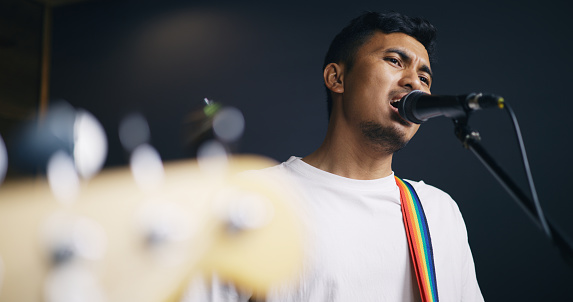 Portrait of Young Asian male musicians in casual clothes playing electric guitar while vocalist singing song into microphone during a rehearsal in studio illumination. Music and entertainment concepts