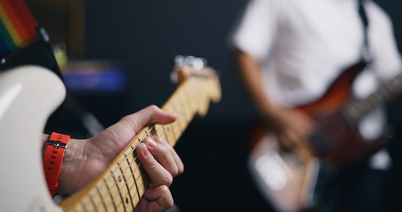Portrait close-up of Young Asian male musicians in casual clothes playing electric guitars while rehearsing in an illuminated studio. Band practice in the studio. Music and entertainment concepts.