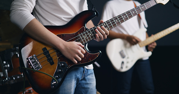 Portrait of Young Asian male musicians in casual clothes playing electric guitars while rehearsing in an illuminated studio. Band practice in the studio. Music and entertainment concepts.