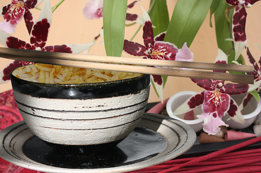 Saffron rice served in a bowl with chopsticks  Orchid in the background  Asian culture
