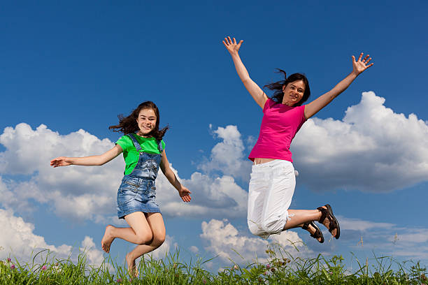 Mother and daughter jumping outdoor against blue sky