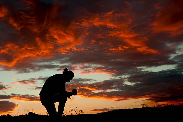 mann prays bei sonnenuntergang - kneeling stock-fotos und bilder