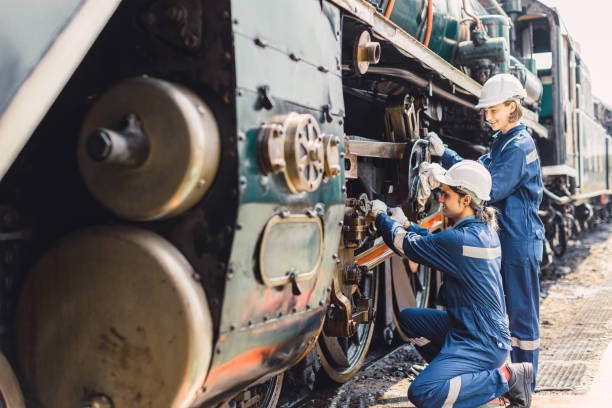 Train engineer team working service maintenance old dirty vintage classic steam engine locomotive in train repair workshop at train station.