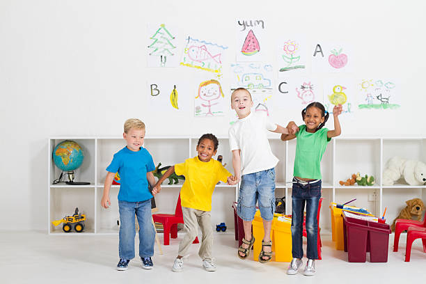 preschool kids jumping group of cheerful preschool kids jumping up in classroom teacher classroom child education stock pictures, royalty-free photos & images