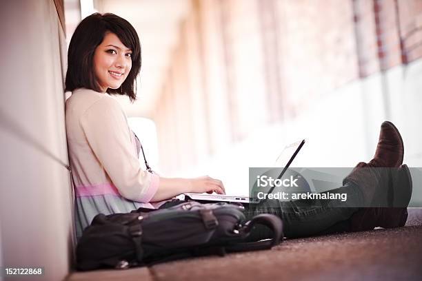 A Woman Using A Laptop While Sitting Against A Wall Stock Photo - Download Image Now