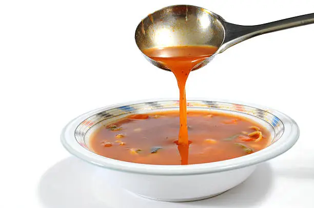 Pouring minestrone soup into a bowl with a ladle isolated on white