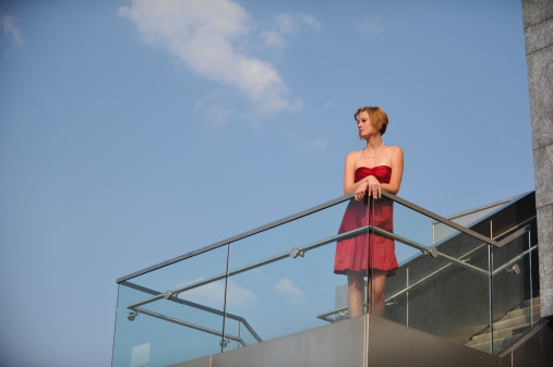 A girl in a red dress leans on a railing against a blue sky in Chattanooga Tennessee near the Art District.