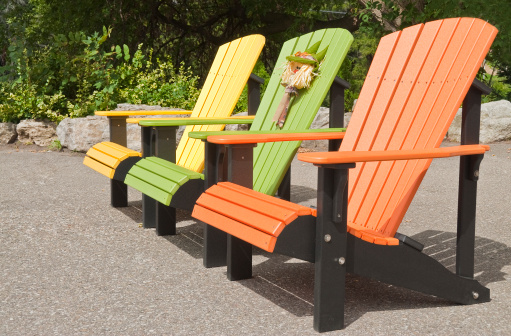 A row of heavy and colorful plastic Adirondack chairs displaying in the sun.