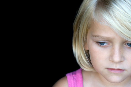Candid shot of a blond sad little girl, looking away fron the camera. Isolated on black, space for text