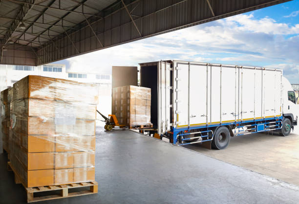 camiones portacontenedores estacionados cargando cajas de paquetes paletas en el muelle del almacén. cadena de suministro, envío de almacén de distribución, cajas de envío de suministros. logística de camiones de carga, transporte de carga. - distribution warehouse fotos fotografías e imágenes de stock