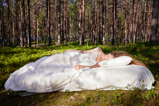 Woman sleeps on a mattress in the summer forest. The girl is resting in nature