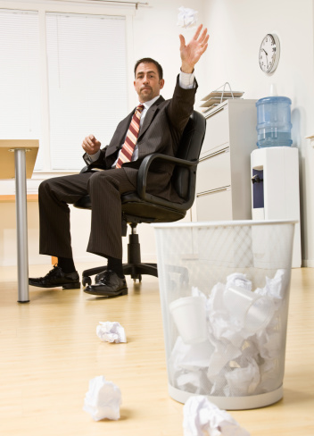 Businessman throwing paper in trash basket in office. Vertical setting.