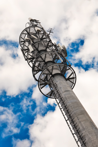 Telecommunication monopole tower with antennas over cloudy sky.