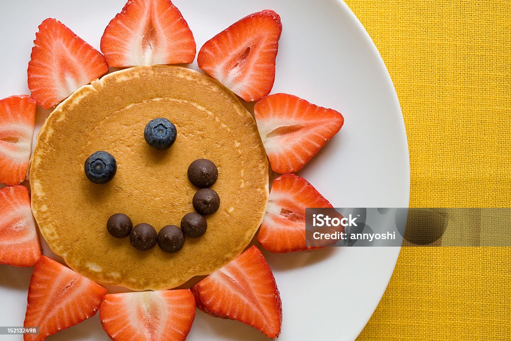 A happy pancake with strawberries and chocolate chips pancake and berries arranged in a smiley face Anthropomorphic Smiley Face Stock Photo