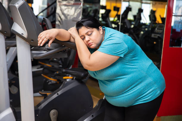 femme indienne fatiguée en surpoids assise sur un tapis roulant au gymnase. - mental health women asian ethnicity bicycle photos et images de collection