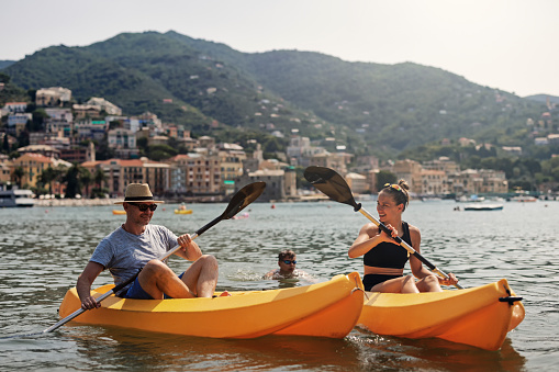 Father and teenage daughter enjoying kayaking in the Ligurian sea on sunny summer day. Mountains and town of Rapallo visible in the background.\nShot with Canon R5