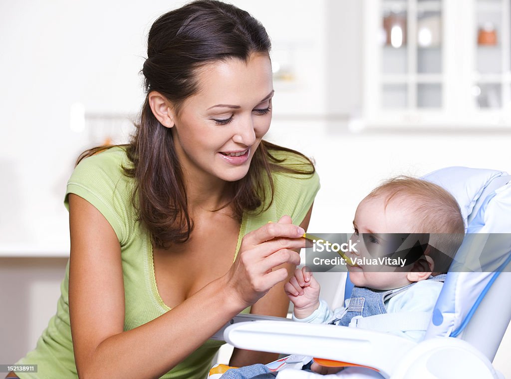 Mother feeding hungry baby Mother feeding hungry baby in the highchair indoors Baby - Human Age Stock Photo
