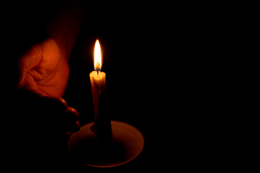 candle flame illuminates a female hand in a room
