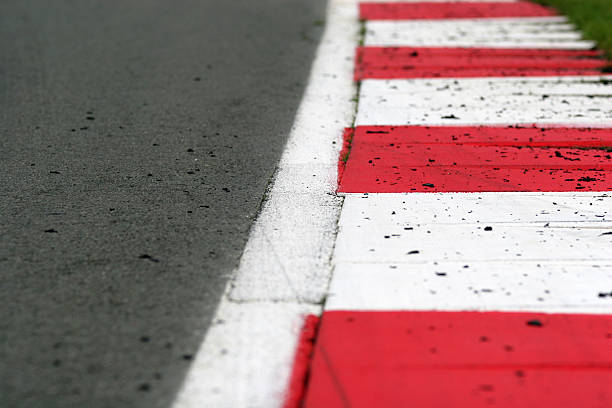 Race Track Kerb with Rubber Debris A brightly painted red and white kerbing edges a smooth tarmac race track. Rubber tyre debris is scattered across the track and kerbs. Shallow depth of field with focus on the second and third stripe. silverstone stock pictures, royalty-free photos & images