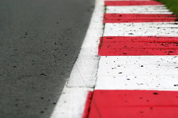 A brightly painted red and white kerbing edges a smooth tarmac race track. Rubber tyre debris is scattered across the track and kerbs. Shallow depth of field with focus on the second and third stripe.