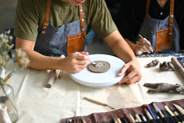 istock Craftspeople wearing aprons working with raw clay, shaping and decorating pottery in workshop. 1521440623
