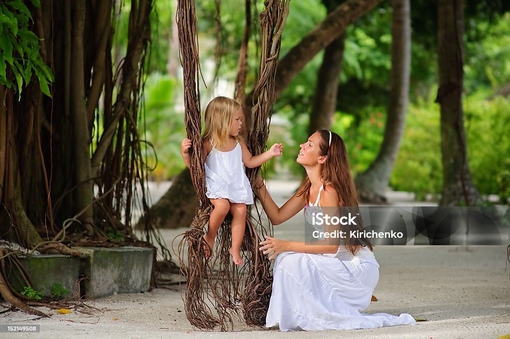 Linda jovem mãe e sua filha pequena no Parque tropical - Foto de stock de Balanço - Equipamento de Playground royalty-free