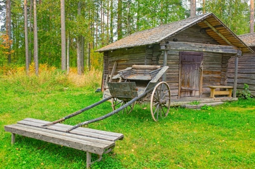 Old wooden cart in front of log barn in autumn forest