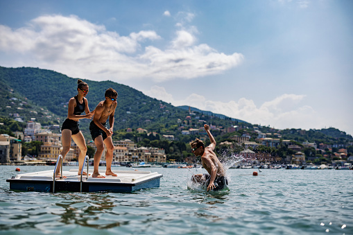 Footage of teenagers playing on a floating platform in the sea in Liguria, Italy\nKids are climbing on the platform and jumping to the sea. In the background there are beautiful mountains , the port and the town of Rapallo.\nShot with DJI Mini Pro 3