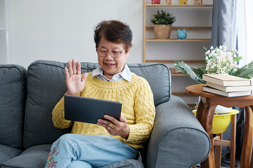 Smiling Asian seniors embrace a fulfilling retirement lifestyle at home, connecting with family through vibrant online video conference calls on their taplet. Radiating happiness and cherishing meaningful interactions, they find joy and well-being in the comforts of their own space.