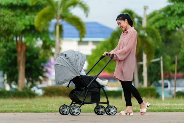 happy mother looking and pushing infant baby stroller while walking in the park