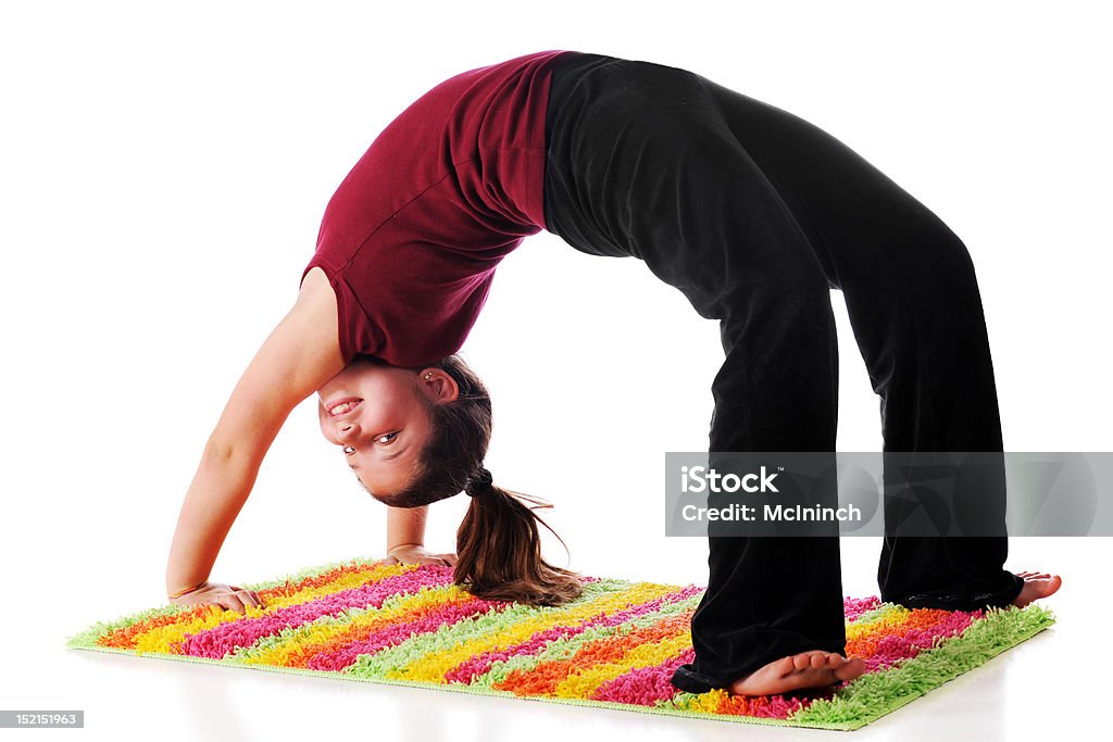 Backbender A happy preteen looking back at the viewer while doing a backbend on a bright,striped rug.  Isolated on white. 10-11 Years Stock Photo