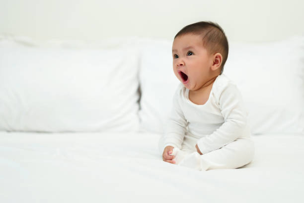 bébé assis et bâillant sur le lit - baby yawning asian ethnicity newborn photos et images de collection