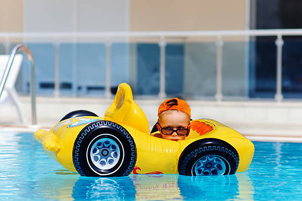 cute toddler boy sits in inflatable car in pool outdoor and have a fun