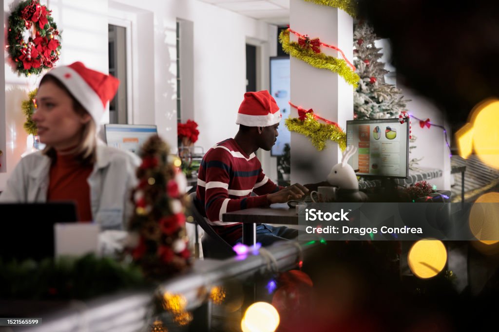 Businessman researches for project Workaholic african american businessman researches for company project in decorated workplace. Tired employee working on data statistics marketing graphs during Christmas holiday season Adults Only Stock Photo